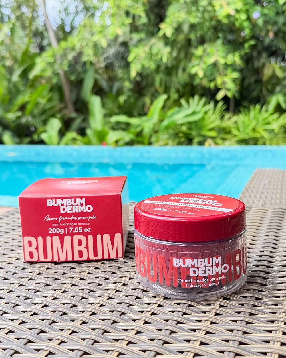 Pote e caixa do creme firmador BumBum Dermo à beira da piscina